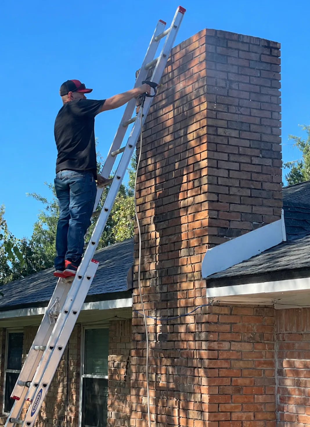 Technician beside an exterior brick chimney and ladder