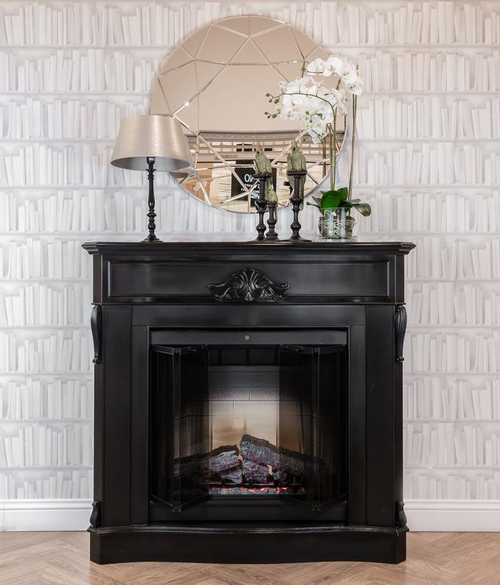 Dark fireplace surround with a mirror, table lamp and floral arrangement